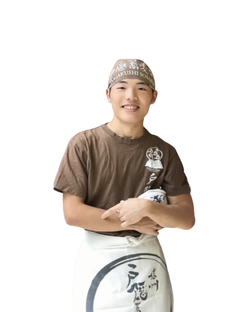 そば358の丸山朝陽さん。戸隠そばのバンダナとエプロンをつけて笑っている